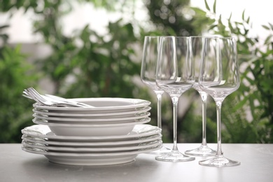 Set of clean dishware, cutlery and wineglasses on grey table against blurred background