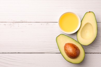 Photo of Cooking oil in bowl and fresh avocados on white wooden table, flat lay. Space for text