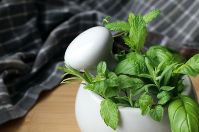 Mortar with different fresh herbs on wooden table, closeup