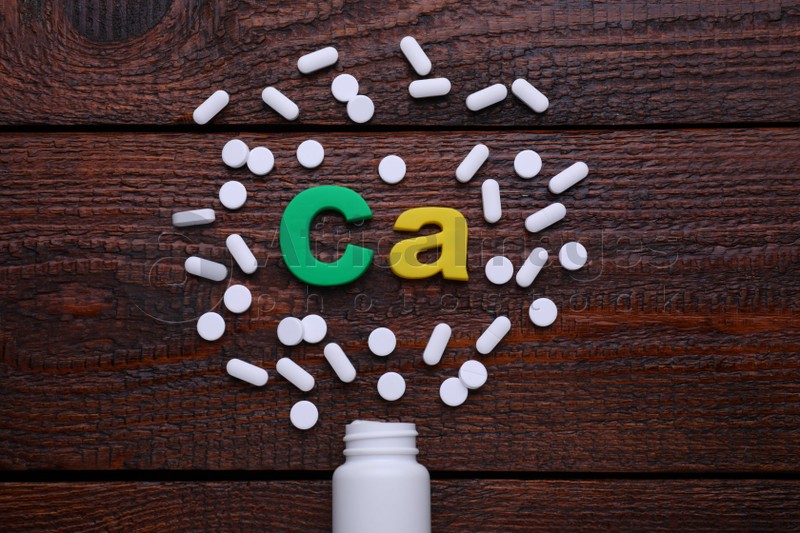 Photo of Paper symbol Ca (Calcium), medical bottle and pills on wooden table, top view
