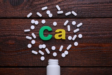 Paper symbol Ca (Calcium), medical bottle and pills on wooden table, top view