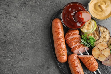 Delicious grilled sausages and vegetables on grey table, flat lay. Space for text