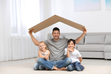 Happy father and his children sitting under cardboard roof at home. Insurance concept
