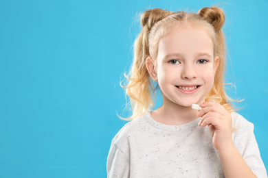 Little girl taking vitamin pill on light blue background. Space for text