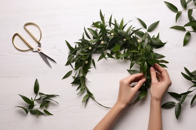 Woman making mistletoe wreath at white wooden table, top view. Traditional Christmas decor