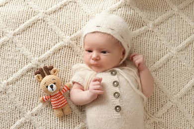 Photo of Adorable little baby with deer toy lying on blanket, top view