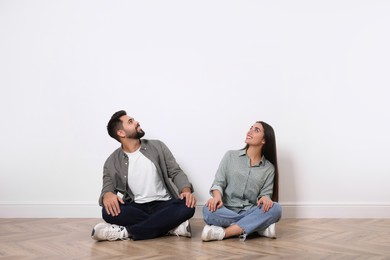 Young couple sitting on floor near white wall indoors