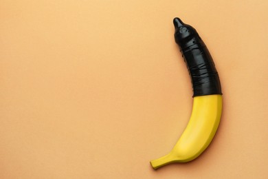 Banana with condom on pale orange background, top view and space for text. Safe sex concept