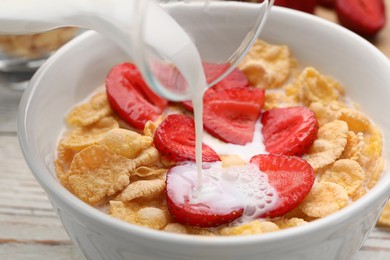 Pouring milk into bowl of tasty crispy corn flakes with strawberries at table, closeup