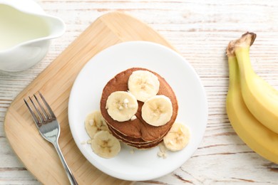 Plate of banana pancakes served on white wooden table, flat lay