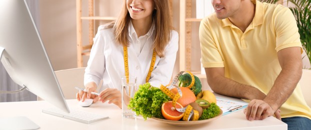 Young nutritionist consulting patient at table in clinic, closeup. Banner design