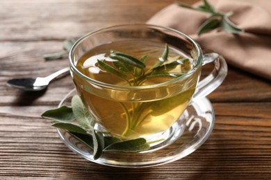 Cup of aromatic sage tea and fresh leaves on wooden table