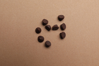 Delicious chocolate chips on brown background, top view