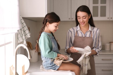 Mother and daughter wiping dishes together in kitchen