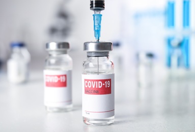 Filling syringe with vaccine against Covid-19 on white table