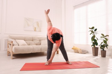 Overweight mature woman doing exercise on yoga mat at home