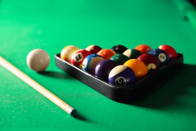 Photo of Plastic triangle rack with billiard balls and cue on green table, closeup