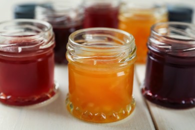 Jars of different jams on white table, closeup