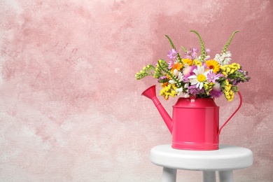 Photo of Watering can with beautiful wild flowers on table against color background