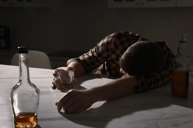 Addicted man with alcoholic drink sleeping at table in kitchen