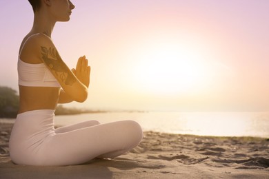 Young woman meditating on beach at sunrise, closeup. Practicing yoga