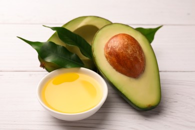 Photo of Cooking oil in bowl and fresh avocados on white wooden table