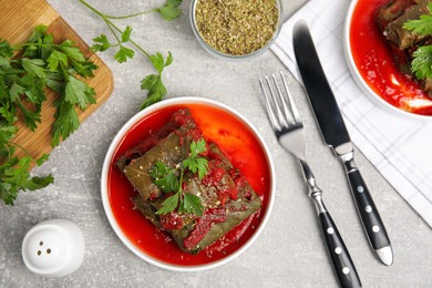 Plate of delicious stuffed grape leaves with tomato sauce, parsley and cutlery on light grey table, flat lay