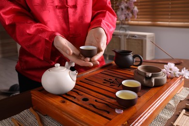 Photo of Master offering cup of freshly brewed tea during traditional ceremony at table, closeup