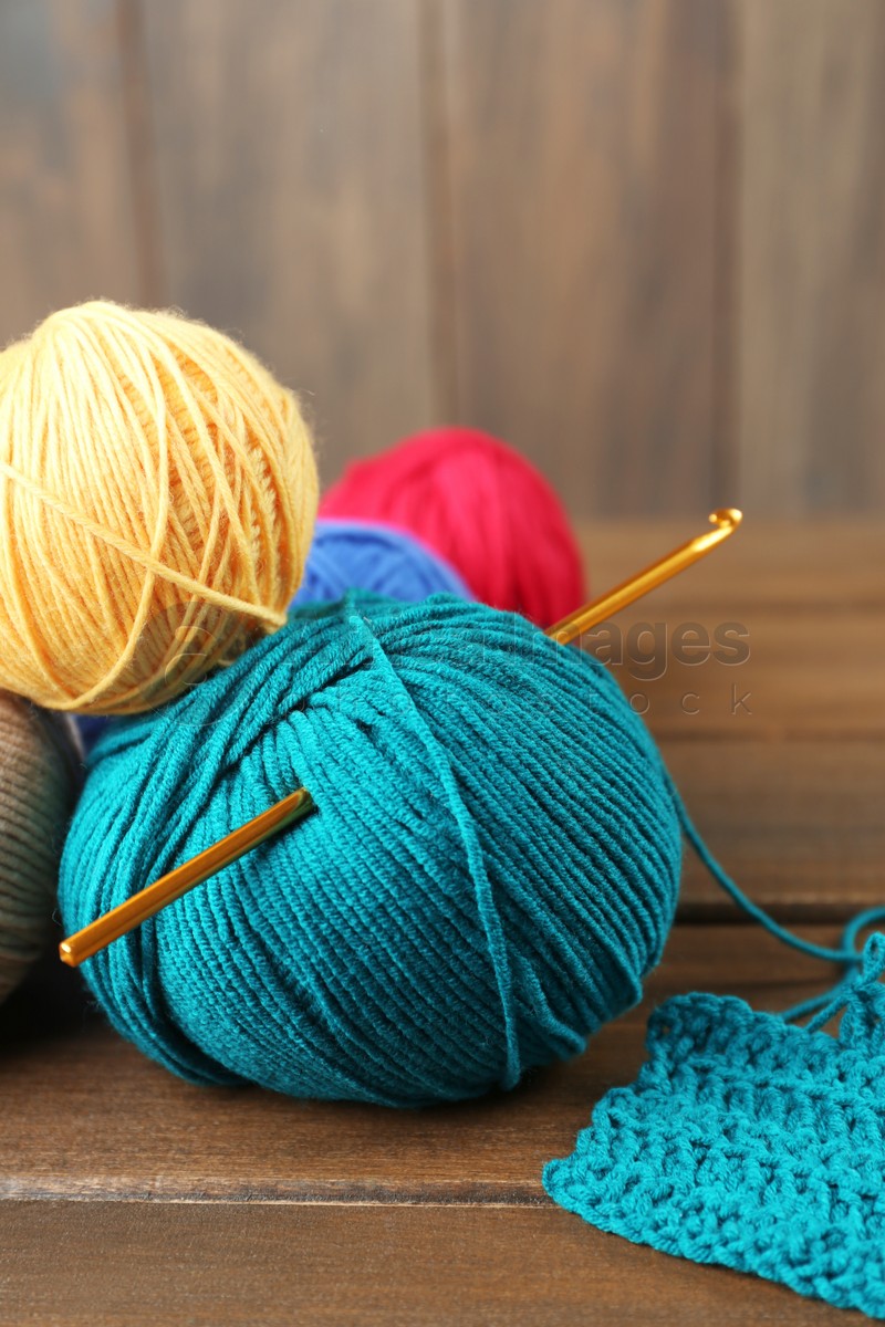 Clews of colorful knitting threads and crochet hook on wooden table