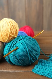 Clews of colorful knitting threads and crochet hook on wooden table