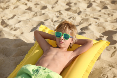 Cute little child with inflatable mattress lying at sandy beach on sunny day