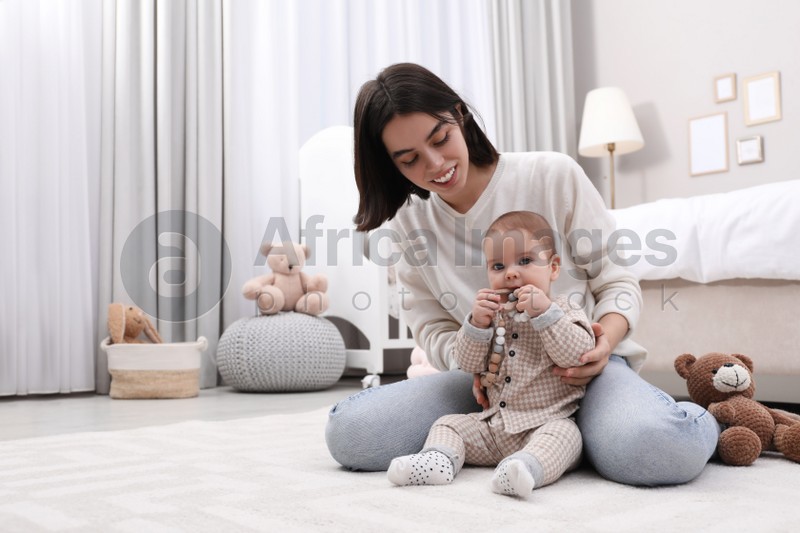 Young mother and her baby with teether on floor at home. Space for text