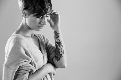 Young woman with tattoo on light background, space for text. Black and white photography