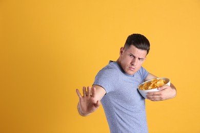 Greedy man hiding bowl with chips on yellow background, space for text