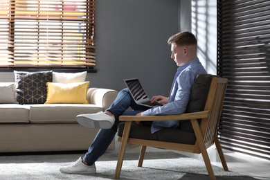 Teenage boy with laptop sitting in armchair at home