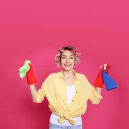 Young housewife with detergent and rag on pink background