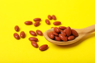 Wooden spoon with pills on yellow background, closeup. Anemia treatment