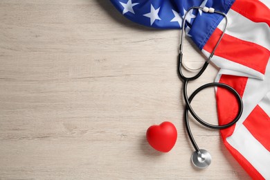 Stethoscope, red heart and American flag on white wooden table, flat lay. Space for text