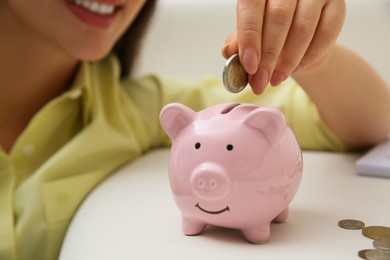 Woman putting coin into piggy bank indoors, closeup. Money savings