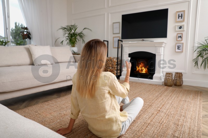 Photo of Young woman watching television at home, back view. Living room interior with TV on fireplace