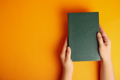 Woman with book on orange background, top view. Space for design