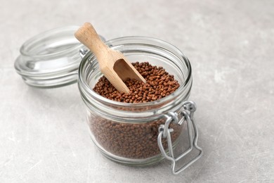 Photo of Glass jar with wooden scoop and buckwheat tea granules on light grey table