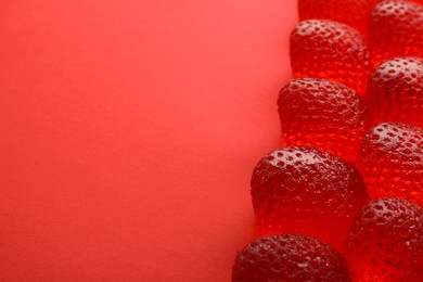 Delicious gummy strawberry candies on red background, closeup. Space for text