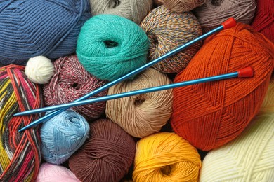 Different balls of woolen knitting yarns and needles as background, top view