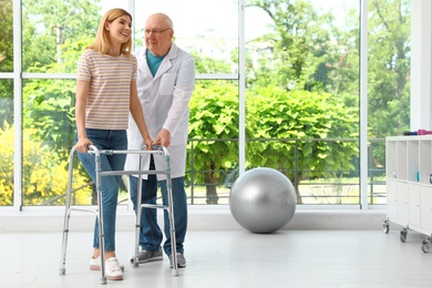 Doctor helping woman with walking frame indoors