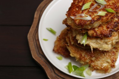Photo of Tasty parsnip cutlets with green onion on wooden table, closeup