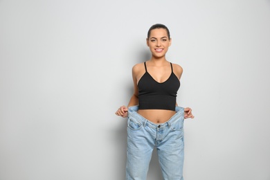 Slim woman in oversized jeans on light background. Weight loss