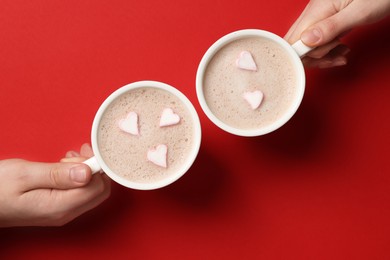 Photo of People holding cups of aromatic coffee with heart shaped marshmallows on red background, top view