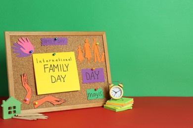 Happy International Family Day. Composition with corkboard, cards and stationery on red table against green background, space for text