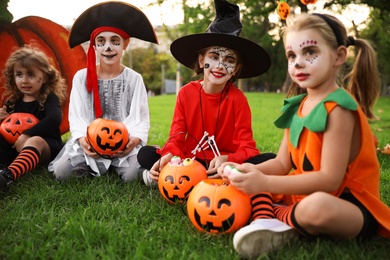 Cute little kids with pumpkin candy buckets wearing Halloween costumes in park